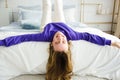 girl lies on the bed upside down in purple sweater and smiles at the camera. concept morning and pampering, childishness