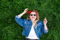 Girl lies on a green lawn, looks at the camera and rejoices. Portrait of a happy, stylish young woman lying on the grass Royalty Free Stock Photo