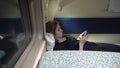 Girl lies in a moving compartment car by the window with a phone in her hands and looks through messengers