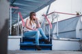 Girl with the light hair sitting on the stairs, spring, sunny warm day, in sunglasses and blue jeans. resting, looking throuth sun Royalty Free Stock Photo