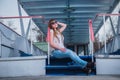 Girl with the light hair sitting on the stairs, spring, sunny warm day, in sunglasses and blue jeans. resting, looking throuth sun Royalty Free Stock Photo