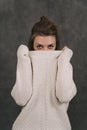 A girl in a light sweater on a gray background. The girl hides her face behind her sweater. The Girl can only see her