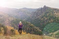 A girl in a lilac jacket looks out into the distance on a mountain, a view of the mountains and an autumnal forest by an overcast Royalty Free Stock Photo