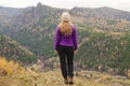 A girl in a lilac jacket looks out into the distance on a mountain, a view of the mountains and an autumnal forest by an overcast Royalty Free Stock Photo