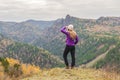 A girl in a lilac jacket looks out into the distance on a mountain, a view of the mountains and an autumnal forest by an overcast Royalty Free Stock Photo