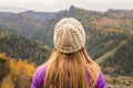 A girl in a lilac jacket looks out into the distance on a mountain, a view of the mountains and an autumnal forest by an overcast Royalty Free Stock Photo