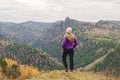 A girl in a lilac jacket looks out into the distance on a mountain, a view of the mountains and an autumnal forest by an overcast Royalty Free Stock Photo