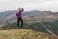 A girl in a lilac jacket looks out into the distance on a mountain, a view of the mountains and an autumnal forest by an overcast Royalty Free Stock Photo