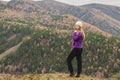 A girl in a lilac jacket looks out into the distance on a mountain, a view of the mountains and an autumnal forest by an overcast Royalty Free Stock Photo