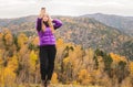 A girl in a lilac jacket makes a salfi on a mountain, a view of the mountains and an autumnal forest by a cloudy day Royalty Free Stock Photo