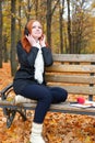Girl listen music on audio player with headphones, sit on bench in city park, autumn season, yellow trees and fallen leaves Royalty Free Stock Photo