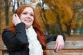 Girl listen music on audio player with headphones, sit on bench in city park, autumn season, yellow trees and fallen leaves Royalty Free Stock Photo