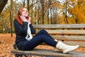 Girl listen music on audio player with headphones, sit on bench in city park, autumn season, yellow trees and fallen leaves Royalty Free Stock Photo