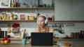 Girl listening music headphones sitting at kitchen with laptop. Woman relaxing. Royalty Free Stock Photo