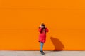 A girl listens to music with headphones on the background of an orange wall . Copy space. Mockup. An article about Royalty Free Stock Photo
