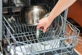 The girl loads dirty dishes into the dishwasher, forks, plates and crutches for washing and disinfection in the kitchen