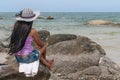 A girl with long black hair blowing in the wind is sitting on the rocks of Hua Hin beach, Thailand, looking out to sea Royalty Free Stock Photo