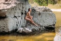 Girl with long blond hair, a slender figure, in a black swimsuit, sits on the rocks near the ocean Royalty Free Stock Photo