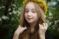 A girl of 13 with long blond hair and a wreath of dandelions. A girl in a spring blooming garden smiling and looking at