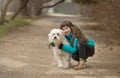 A girl with long brown hair aged 9 years in a sports blue jacket and black jeans with a white furry dog,