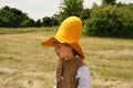 Girl wearing the high yellow farmer hat with the wide brim is walking in the green fields in summer. Fileds in the background Royalty Free Stock Photo