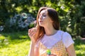 A girl with long brunette hair blows bubbles blower in the summer on a green meadow on a sunny day Royalty Free Stock Photo