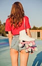 Girl with long dark hair is back with roller skates on her shoulder. Warm summer evening in the skate park. Royalty Free Stock Photo