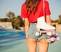 Girl with long dark hair is back with white roller skates on her shoulder. Warm summer evening in the skate park. Outdoor. Close Royalty Free Stock Photo