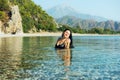 A girl with long dark hair swims in the sea on a beautiful deserted beach with green mountains along the banks.