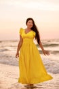 A girl in a long dress with long black hair walks at dawn along a deserted beach