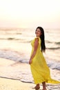 A girl in a long dress with long black hair walks at dawn along a deserted beach