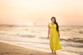 A girl in a long dress with long black hair walks at dawn along a deserted beach