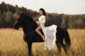 Girl in a long dress riding a horse, a beautiful woman riding a horse in a field in autumn. Country life and fashion, noble steed Royalty Free Stock Photo