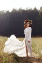 Girl in a long dress stands in a field with a wreath on her head and a bouquet of flowers in her hands, a beautiful woman in the Royalty Free Stock Photo