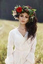 Girl in a long dress stands in a field with wreath on her head and bouquet of flowers in her hands, beautiful woman in the rays of Royalty Free Stock Photo