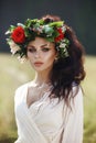 Girl in a long dress stands in a field with wreath on her head and bouquet of flowers in her hands, beautiful woman in the rays of Royalty Free Stock Photo