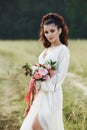 Girl in a long dress stands in a field with wreath on her head and bouquet of flowers in her hands, beautiful woman in the rays of Royalty Free Stock Photo