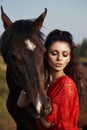 Girl in a long dress stands near a horse, a beautiful woman strokes a horse and holds the bridle in a field in autumn. Country Royalty Free Stock Photo