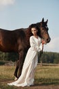 Girl in a long dress stands near a horse, a beautiful woman strokes a horse and holds the bridle in a field in autumn. Country Royalty Free Stock Photo
