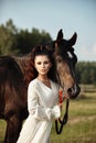 Girl in a long dress stands near a horse, a beautiful woman strokes a horse and holds the bridle in a field in autumn. Country Royalty Free Stock Photo