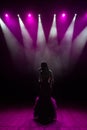 Girl in long gown performing on stage. Girl singing on the stage in front of the lights. Silhouette of singer standing