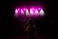 Girl in long gown performing on stage. Girl singing on the stage in front of the lights. Silhouette of singer standing Royalty Free Stock Photo