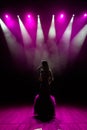 Girl in long gown performing on stage. Girl singing on the stage in front of the lights. Silhouette of singer standing Royalty Free Stock Photo