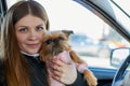 Girl with long hair in a black jacket and a small dog in pink clothes near window of a car Royalty Free Stock Photo