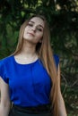 A girl with long hair, blonde, stands near a fir tree and looks at the camera with a grin, in a blue blouse. Royalty Free Stock Photo