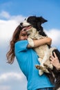 A girl with long hair in a blue T-shirt holds a black and white border collie dog in her arms. Portrait against a bright Royalty Free Stock Photo