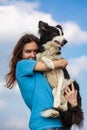 A girl with long hair in a blue T-shirt holds a black and white border collie dog in her arms. Portrait against a bright Royalty Free Stock Photo