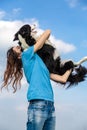 A girl with long hair in a blue T-shirt holds a black and white border collie dog in her hands. Portrait against a Royalty Free Stock Photo