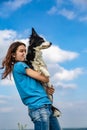 A girl with long hair in a blue T-shirt holds a black and white border collie in her arms. Portrait against a bright Royalty Free Stock Photo