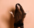 Girl with long hair in brown turtleneck, short skirt, nylon tights. Smiling, gesticulating posing on beige background. Close up